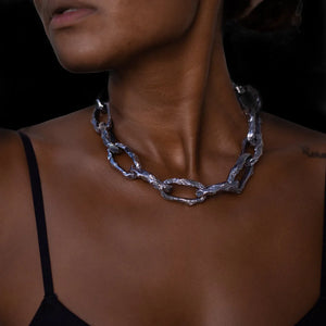 Woman wearing the Aji XL thick chain necklace featuring large, textured silver links against dark skin, shown with a black top.