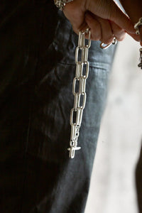 Close-up of a hand holding a bold chunky chain with large rectangular silver links, hanging down against a dark background.