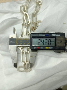 A digital caliper measuring the width of a chunky chain necklace, displaying 24.20 mm, placed on a white fabric background.