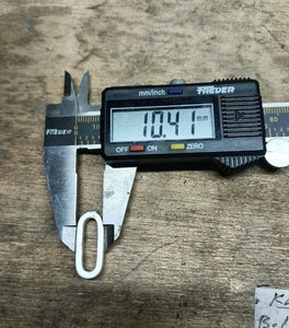 Close-up of a digital caliper measuring a link for a chunky chain, displaying 10.41 mm on the screen, placed on a wooden surface.