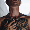 Person wearing a Gopa big chain necklace with a circular ring centerpiece, holding the chain against their chest, showing detailed tattoos.