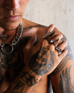 Man wearing a Gopa bold chunky chain necklace with circular pendant, displaying detailed hand tattoos and chunky rings.