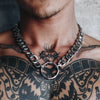 Close-up of a man wearing a Gopa chunky chain necklace with a large circular centerpiece over his tattooed chest.