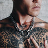 Man wearing a Gopa thick chain necklace with a large circular centerpiece visible over his tattooed chest.