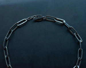 Close-up of a large black chain with rectangular links arranged in a semi-circle, placed against a dark background.