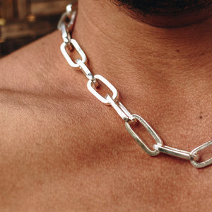 Close-up of a silver thick chain necklace with large rectangular links resting on a person's bare neck.