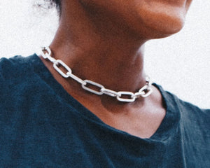 Close-up of a woman wearing a thick chain necklace with large rectangular silver links paired with a dark blue top.