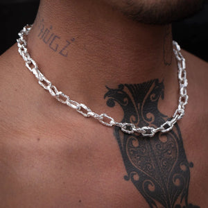 A close-up of a man’s neck adorned with the Ula chunky chain, a textured silver necklace, with visible tattoos on his neck and chest.