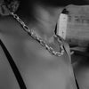 Woman wearing Ula silver heavy chain with textured links, shown in black and white, highlighting the necklace around her neck.