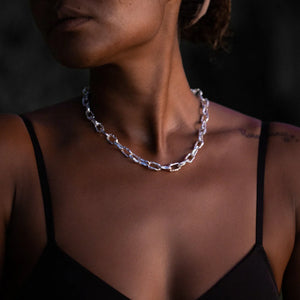 A woman wearing the Ula women's chunky chain necklace with silver textured links and a visible tattoo on her shoulder.