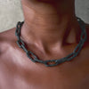 Close-up of a Ula X chunky chain necklace in oxidized silver, featuring large, textured links, worn around the neck.