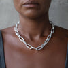 Close-up of a person wearing the Ula X thick chain necklace featuring large, textured silver links that stand out against the wearer's skin.