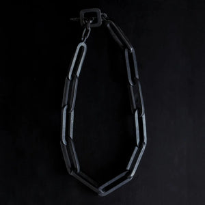 XL black chunky chain necklace with large rectangular links and a square clasp, arranged in a loop against a dark background.