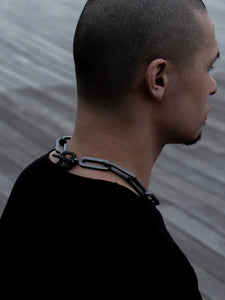 Side profile of a man wearing an XL heavy chain necklace with large rectangular links, paired with a black shirt, in an outdoor setting.